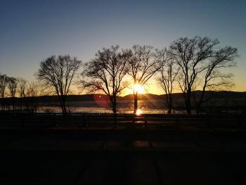 Sunset over Rt 9A, Rt 9, trees, train tracks, Hudson River, and the distant shore